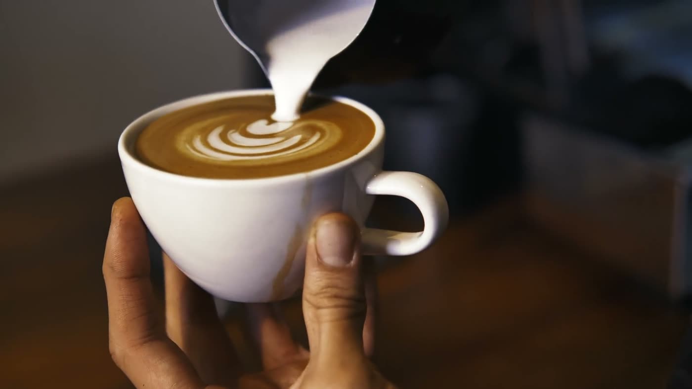 A barista pouring latte art into a white cup